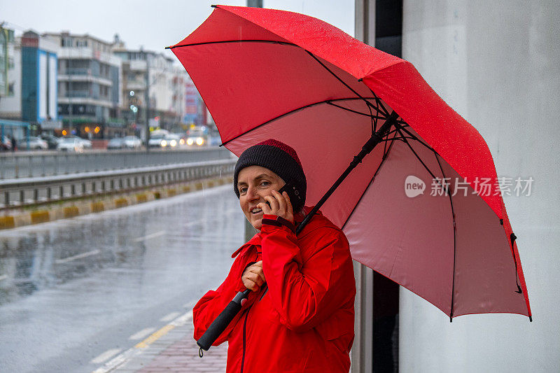 一位女士在雨天撑着伞在公共交通车站等车