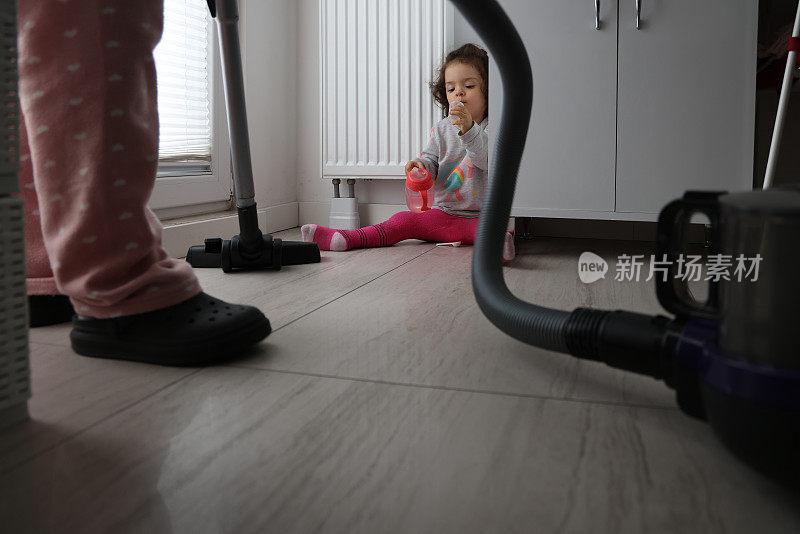 女人在用吸尘器打扫，小女孩坐在地板上