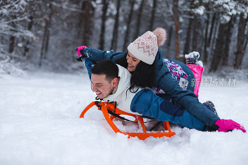 年轻美丽浪漫的夫妇躺在雪橇上在雪地里玩得很开心