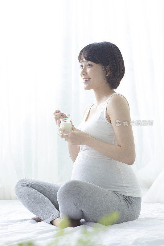 孕妇拿着优格盘腿坐着微笑