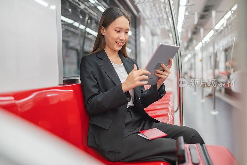 一名年轻的亚洲女商人的肖像照片旅行在通勤火车和红色行李在她的平板电脑上观看视频在旅程过境的商务旅行