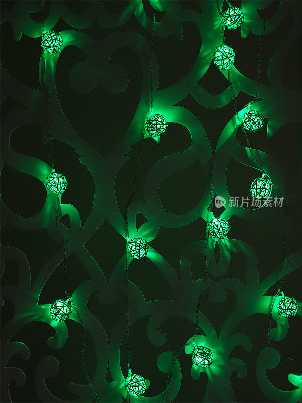 绿色藤球圣诞灯花环在黑暗的背景。圣诞节或新年的绿色灯花环在图案墙上。模糊发光的灯泡花环。垂直的照片。