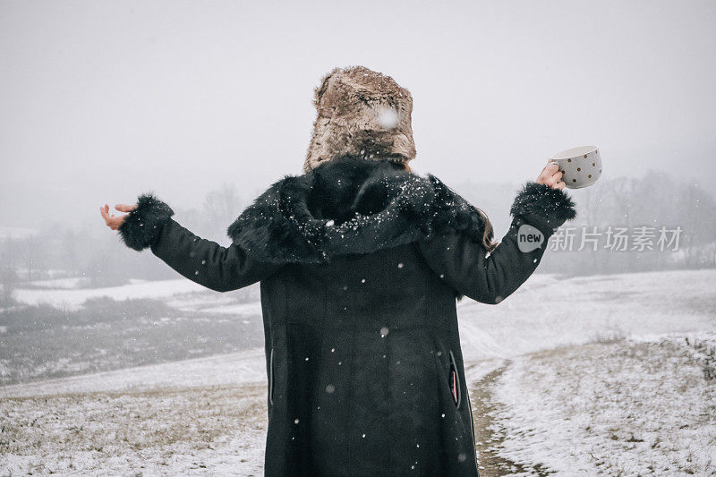 站在雪地上拿着一杯茶的年轻女子