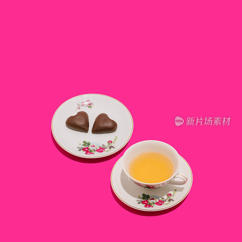 复古的浪漫成分的复古杯茶和两个巧克力心形在生动的粉红色背景。最小限度的爱或情人节的想法。