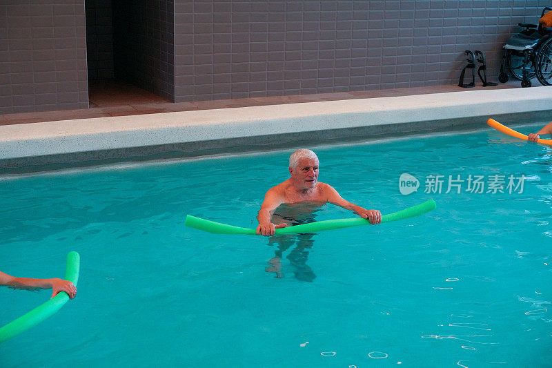 老年男子帕金森病患者在游泳池里与漂浮的蠕虫一起运动。
