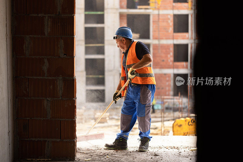 无法辨认的中年建筑工人正在用扫帚清理工地上的灰尘