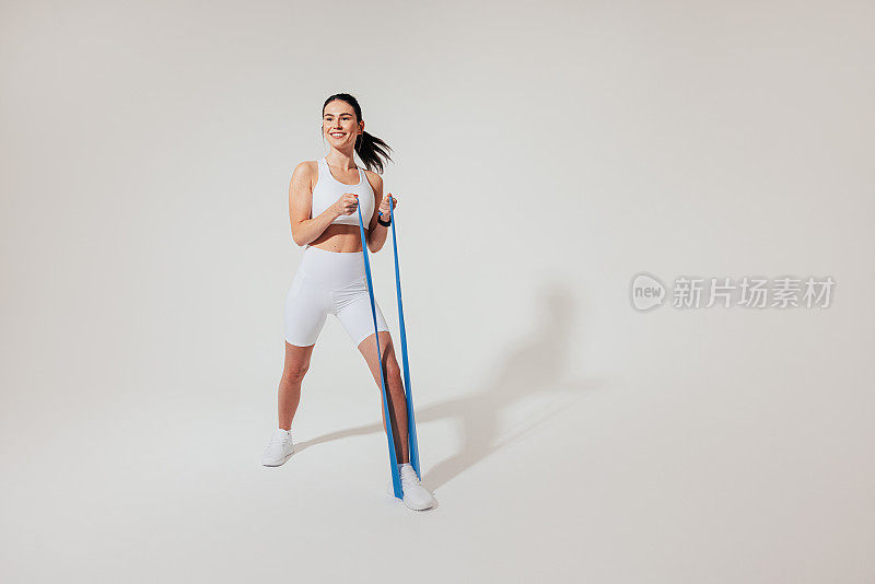 一名身穿白色健身服的积极女性正在用抵抗带热身手臂