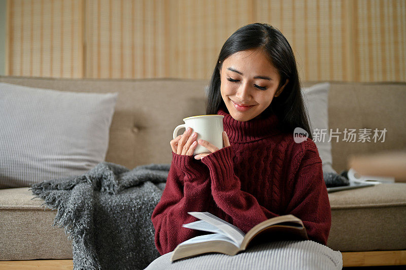 一个放松的亚洲女人在客厅里一边喝咖啡一边看书