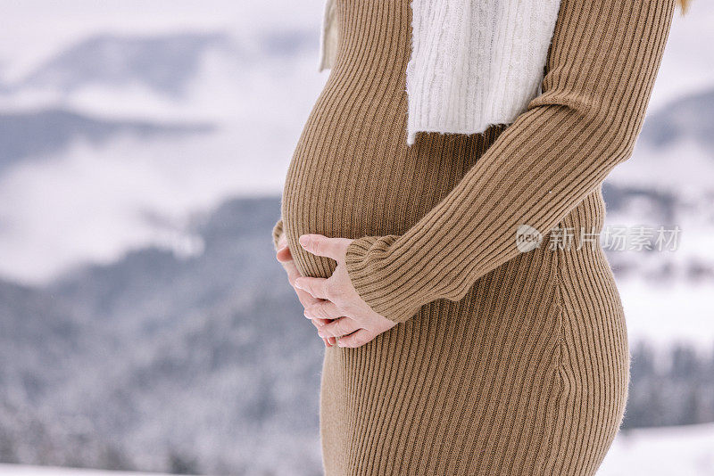 穿着保暖衣服的女人抚摸着她怀孕的肚子