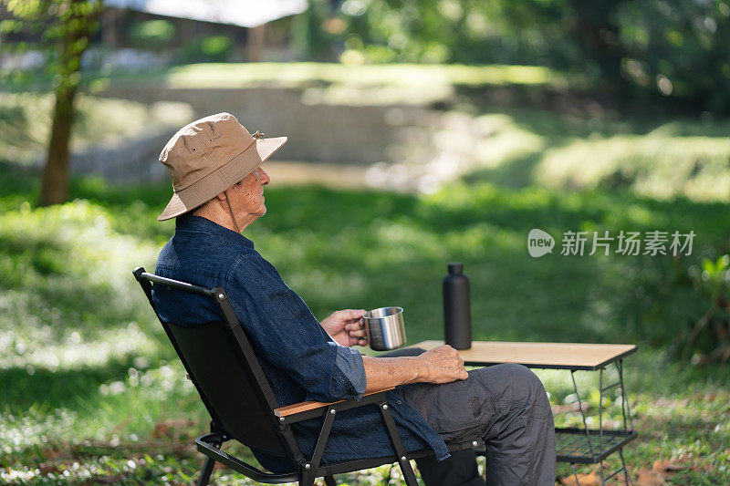 一位亚洲老人用不锈钢杯喝着咖啡享受大自然