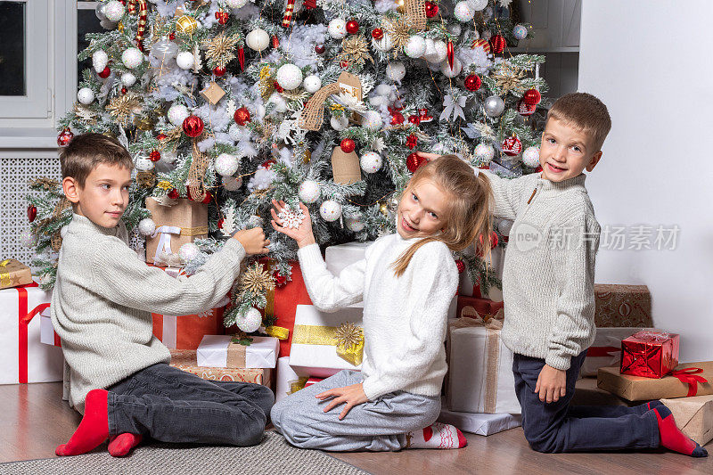 可爱欢快的孩子们，男孩和女孩在家里装饰圣诞树，挂球，花环。