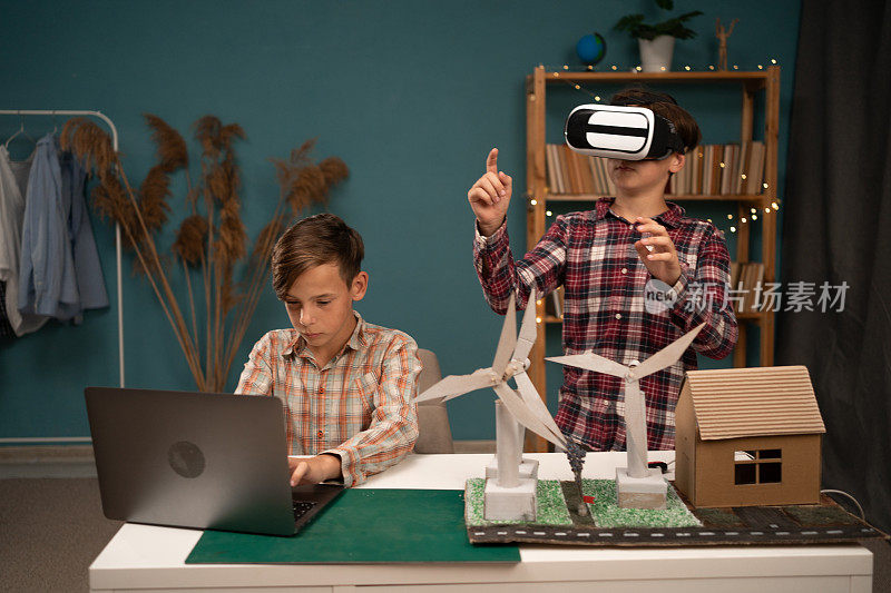 小学生在家里做一个关于可再生能源的项目，一个戴着虚拟眼镜的男孩拿着一个风力涡轮机模型，另一个孩子用笔记本电脑工作。一群学生为未来做计划