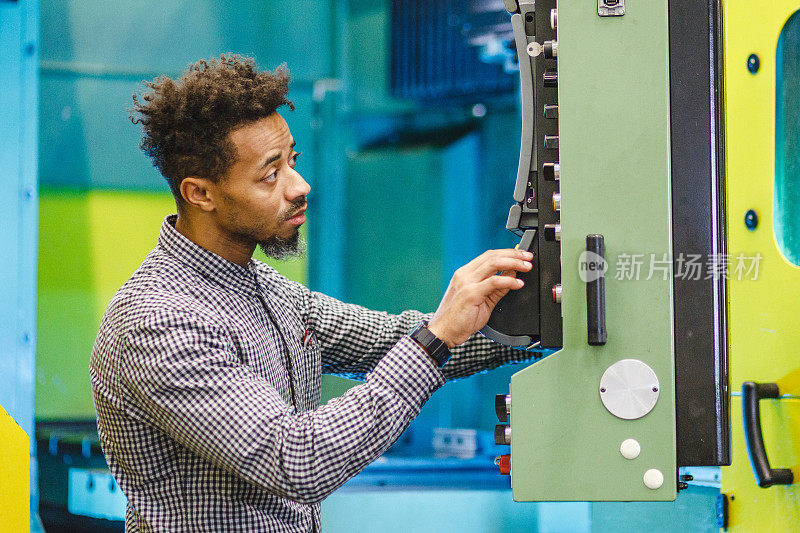 专注的成年男性混合电气工程师在工厂里按下数控机床控制面板上的按钮
