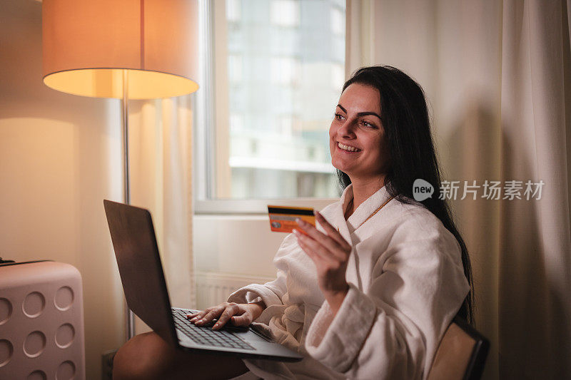 微笑的年轻女子在酒店房间里用笔记本电脑购物