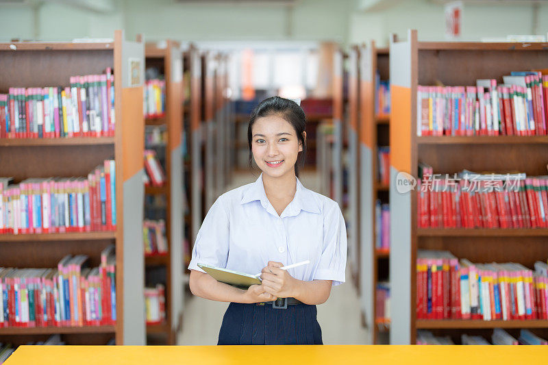 长发亚洲女学生半身照站在图书馆中间拿着iPad和笔，准备高考在名校学习