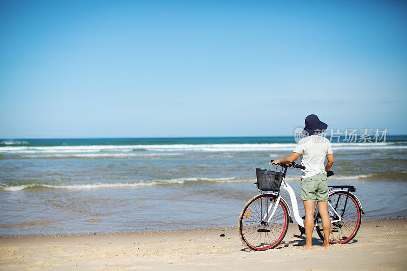 年轻的成年女子骑着自行车在海滩上
