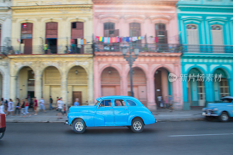 古巴哈瓦那，一辆蓝色的老爷车驶过五颜六色的建筑