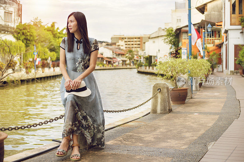 亚洲女游客坐在马六甲河畔放松，欣赏美丽的风景，在傍晚日落的时刻