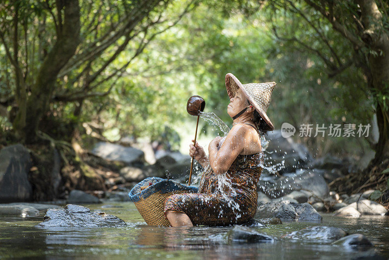 在农村生活的老年妇女农民农村里，Asaia老太太在河溪自然上淋浴