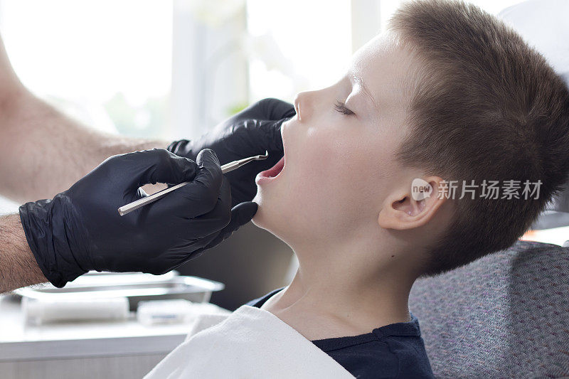 牙科医生为孩子检查牙齿。那个男孩张着嘴坐在牙科椅上。戴着黑色手套的牙医手里拿着挖掘机。