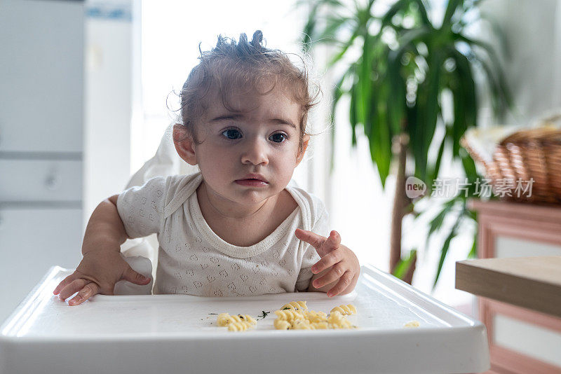 蹒跚学步的小女孩坐在喂食椅上吃食物
