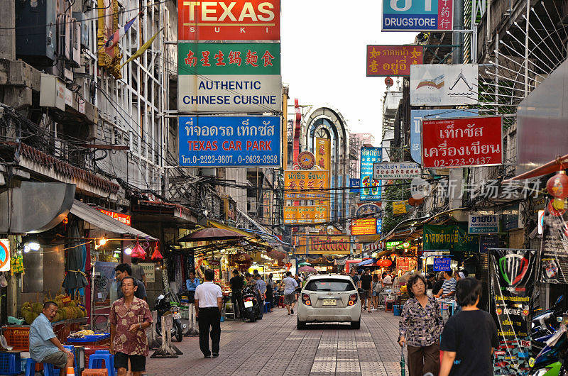 人们，汽车，带有彩色广告和标志的商店和餐馆在中国城的一条街上。曼谷泰国