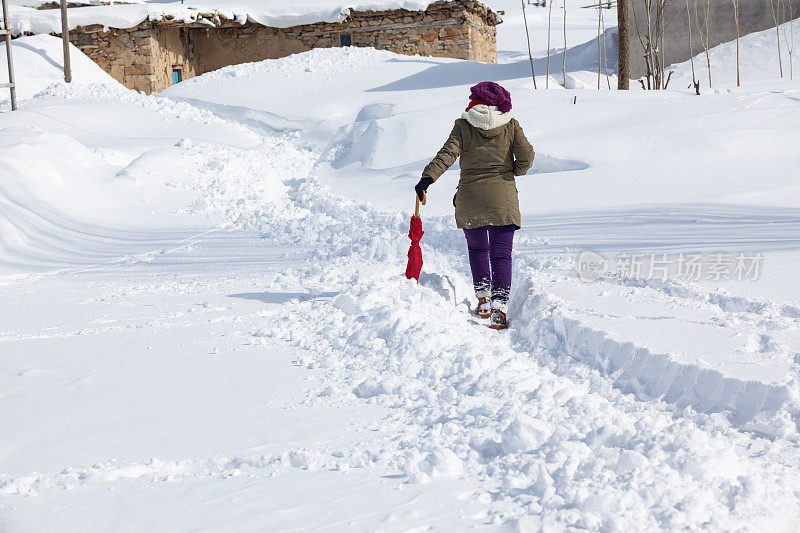 成年妇女穿着暖和的衣服在雪地上行走在农村