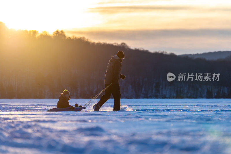 冬天日落时分，爷爷拉着孙子在冰湖上的雪橇