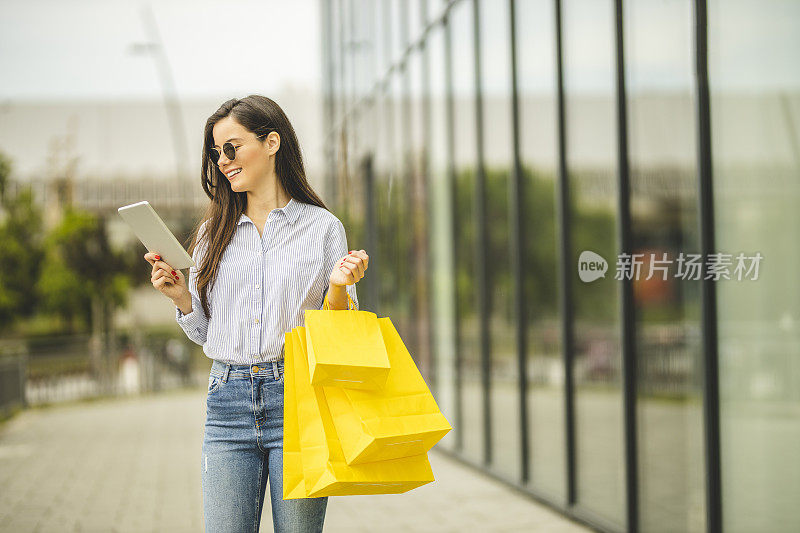 年轻漂亮的女人提着购物袋，用着平板电脑，走路