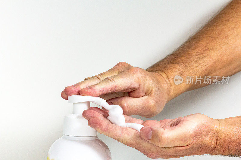 用肥皂洗手。湿男人的手满是起泡的肥皂，推着肥皂泵。