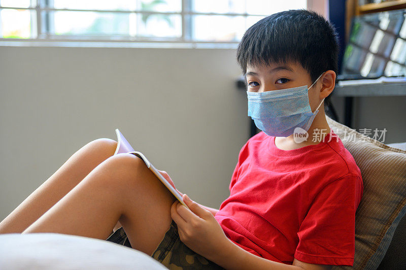 亚洲男孩戴着外科口罩在家学习