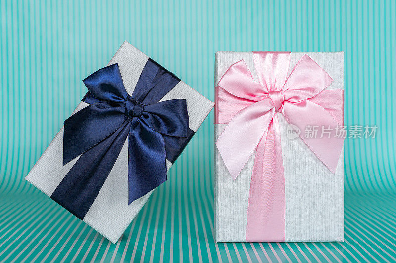 两个白色礼品盒与粉红色和蓝色丝带在一个绿松石条纹背景股票照片