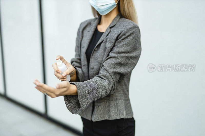 这是年轻女商人在冠状病毒大流行期间用洗手液洗手并佩戴防护口罩以保护自己的特写