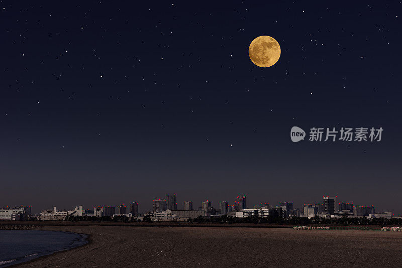 从海滩上看到的城市天际线上升起的满月
