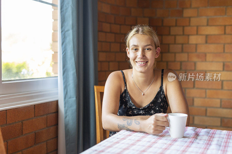 年轻女子坐在餐桌旁，喝一杯茶或咖啡