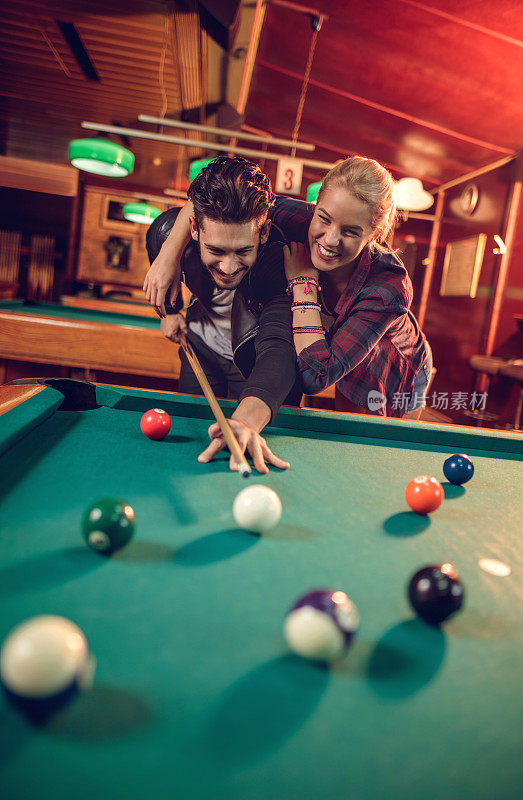 一对年轻的情侣在酒吧打台球的时候玩得很开心。