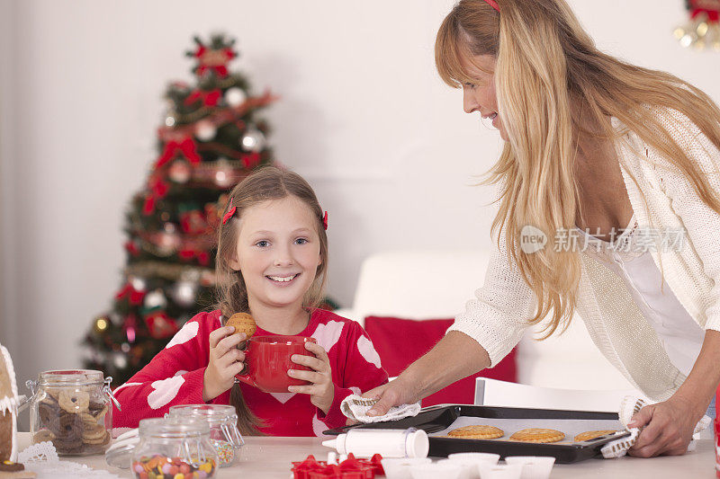 妈妈和女儿在圣诞树旁拿着饼干。