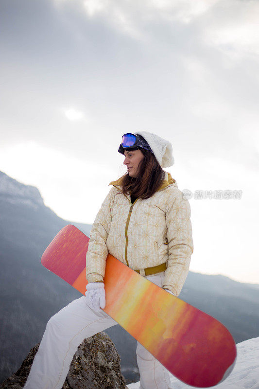 女人拿着滑雪板，背景是高山