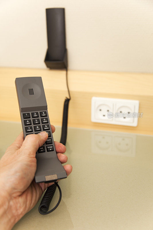 现代化的旅馆房间里有电话。人的手在按按钮。