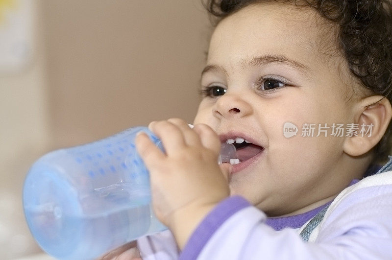 微笑的一岁小女孩喝她的瓶子