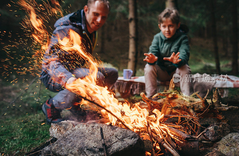 父亲和儿子在森林里的篝火旁取暖
