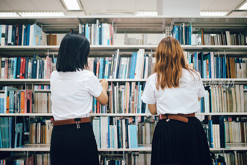 两个年轻的亚洲学生在图书馆找书