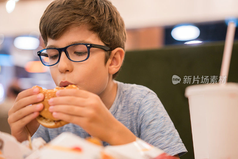 可爱健康的学前班小男孩坐在户外咖啡馆里吃汉堡