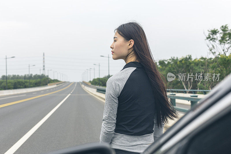 穿着运动服的漂亮女人靠在汽车引擎盖上