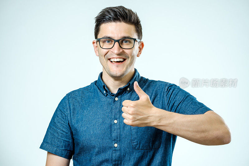 年轻的白人男子与眼镜显示拇指向上手势在灰色的背景
