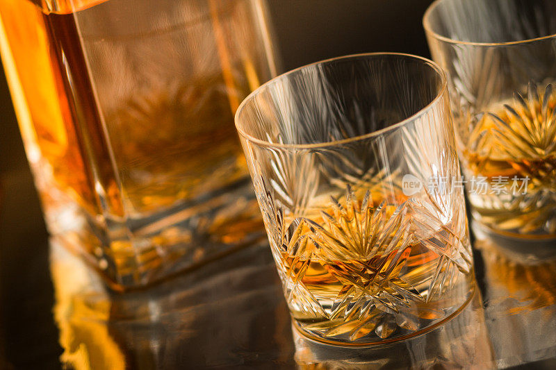 近距离与麦芽苏格兰威士忌在反射吧台与滗水器的背景上的优良水晶玻璃杯