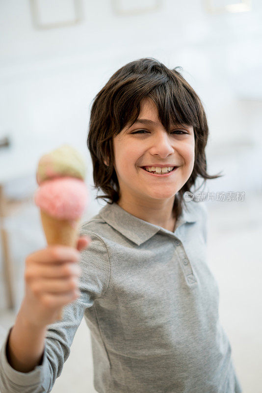 一个漂亮的小男孩的肖像拿着他的冰淇淋非常高兴和微笑