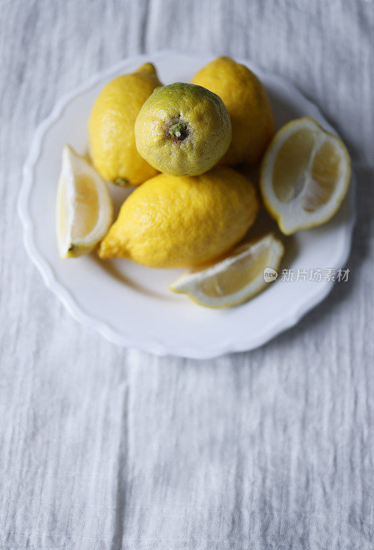 白色桌布上，白色盘子上放柠檬和柠檬片，正面