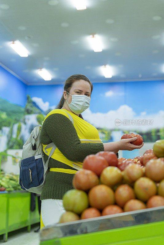 年轻的妇女抱着她的孩子在超市的水果和蔬菜选择他们的食物时看着相机的肖像