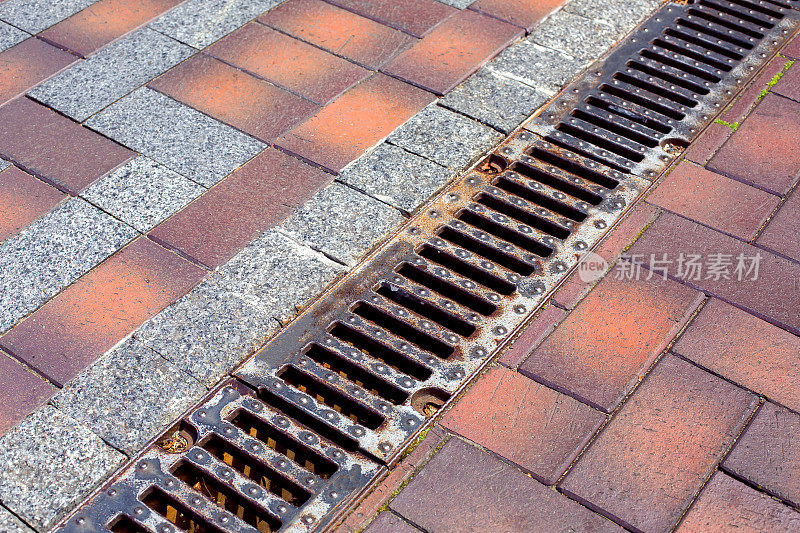 一个排水沟渠覆盖着一个铁格栅，在人行道上由石头瓷砖和花岗岩石头制成，这是一个雨水排水系统的特写，从铺好的道路。